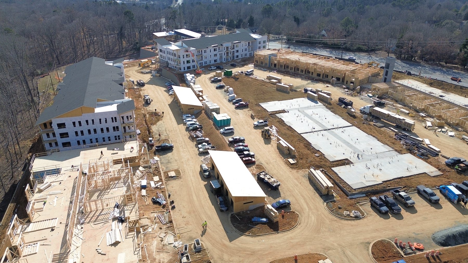 Aerial view of a multifamily development under construction with buildings at framing, dry-in, and slab stages