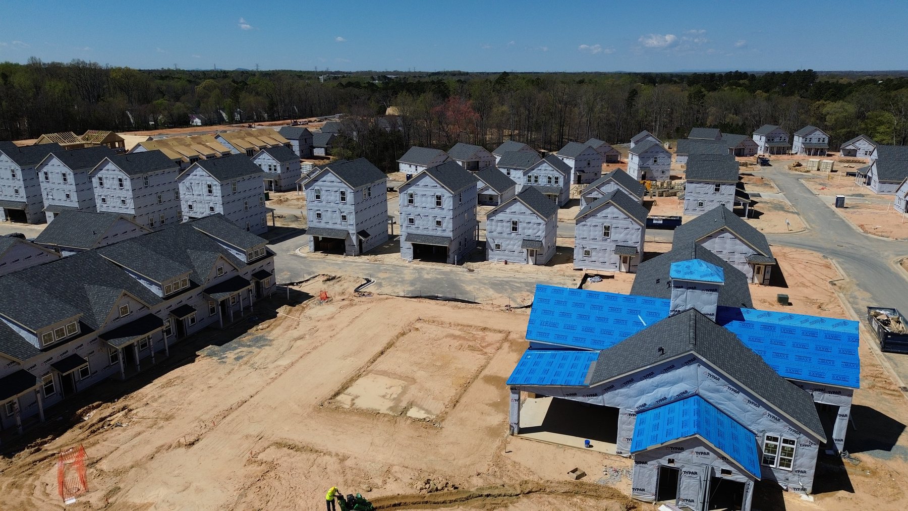 Aerial view of a single-family subdivision under construction with homes at framing, house wrap, and roofing stages